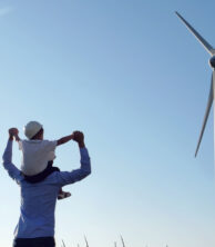 Child on adult's shoulders with a windmill in the background
