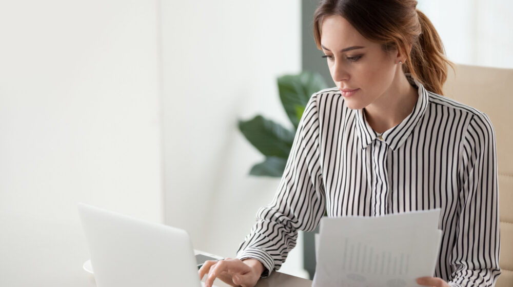 Woman on laptop holding paper