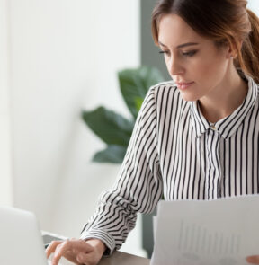 Woman on laptop holding paper